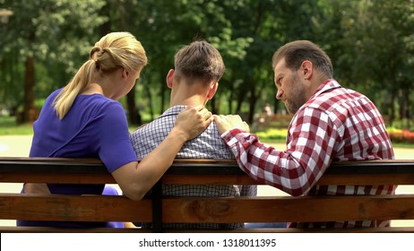 Caring Mother And Dad Supporting Sad Teen Son Sitting On Bench In Park, Crisis