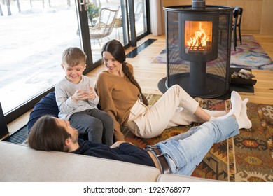 Caring Mother. Full Length View Of The Nice Dark Haired Woman Smiling While Sitting At The Carpet With Her Husband And Child. Family Warming Near The Fireplace