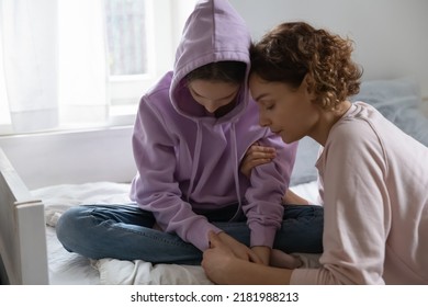 Caring mother hugging, comforting depressed upset teenage daughter, stressed unhappy teenager girl wearing hood sitting on bed, thinking about problems, feeling lonely and misunderstood - Powered by Shutterstock