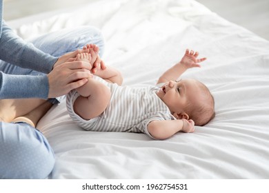 Caring Mother Making Gymnastics To Her Newborn Baby On Bed At Home, Unrecognizable Woman Helping Infant Kid To Relief Gas, Doing Exercises With Little Kid To Prevent Child Constipation, Cropped Image