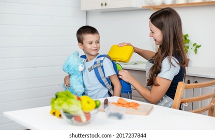 Caring mother puts yellow plastic lunch box to her son in a school backpack. School food or lunch, concept image. - Powered by Shutterstock