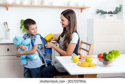 Caring Mother Puts Yellow Plastic Lunch Box To Her Son In A School Backpack. School Food Or Lunch, Concept Image.