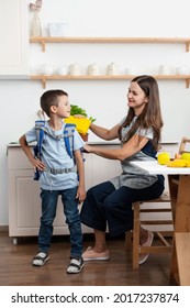 Caring Mother Puts Yellow Plastic Lunch Box To Her Son In A School Backpack. School Food Or Lunch, Concept Image.