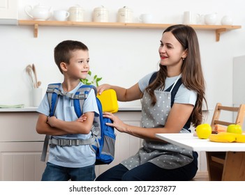 Caring Mother Puts Yellow Plastic Lunch Box To Her Son In A School Backpack. School Food Or Lunch, Concept Image.