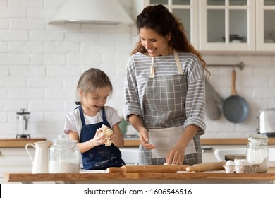 Caring mother and small adorable daughter cooking together in kitchen, mom teaches cute kid girl kneading dough for domestic pie preparing surprise for family, enjoy process and communication concept - Shutterstock ID 1606546516