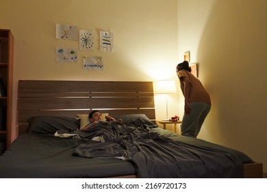 Caring Mother Turning Off Lamp On Bedside Table In Room On Her Sleeping Son