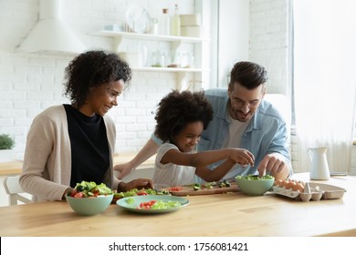 Caring Multiethnic Couple Teach Small Daughter Cook Vegetable Salad In Modern Domestic Kitchen. Family Enjoy Cooking And Communication Together, Healthy Organic Food Preparation, Love And Bond Concept