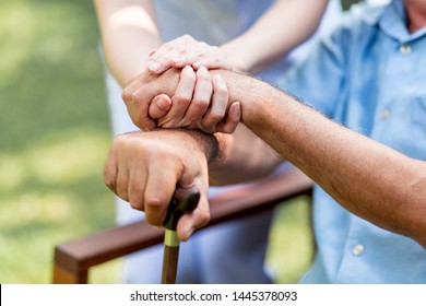 Caring Nurse Helping Senior Man Sitting On Bench In Gaden. Asian Woman, Caucasian Man. Holding Hands With Cane, Close Up.