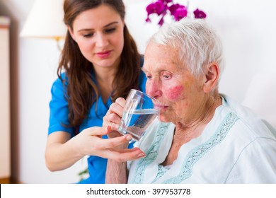 Caring nurse helping sick elderly woman to drink in bed in a nursing home.