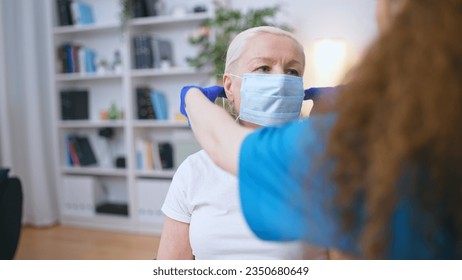 Caring nurse helps senior woman put her protective face mask on, assisted living facility - Powered by Shutterstock