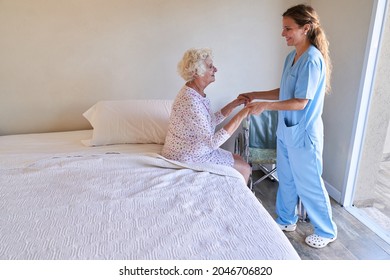 Caring Nurse Helps Sick Senior Woman Get Up From Bed In Nursing Home