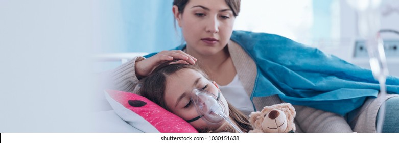 Caring older sister supporting a girl wearing an oxygen mask in a health center