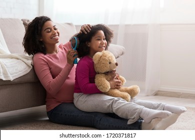 Caring Pregnant African Mom Combing Her Little Daughter's Hair At Home, Sitting Together On Floor In Living Room, Free Space