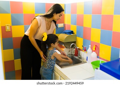 Caring preschool teacher with a little girl student teaching her how to wash her hands and good hygiene in the bathroom - Powered by Shutterstock