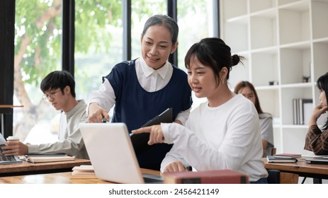 A caring and professional mature Asian female teacher or professor is teaching students in the classroom, helping and explaining a difficult question to a student. education concept
