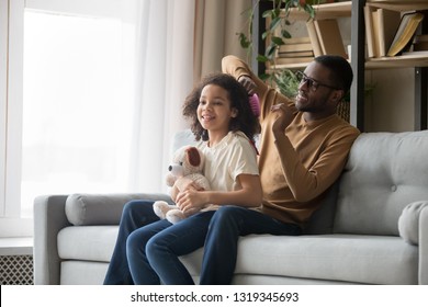 Caring single african dad baby sitter brushing doing daughter afro hair sitting on sofa, loving black father help child with hairstyle combing in the morning at home, family daddy kid bonding concept - Powered by Shutterstock
