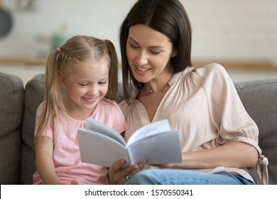Caring single parent young adult mother and happy cute little preschool child daughter reading book learning education fairy tale story bonding enjoying family lifestyle hobby at home sit on sofa