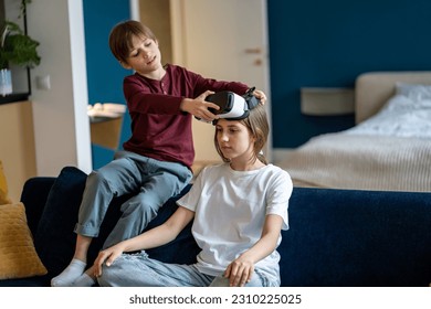 Caring small brother help teenage girl put on virtual reality glasses. Curious older sister with child boy prepare immersive in 3D video game with goggles. Interested siblings use VR headset together. - Powered by Shutterstock