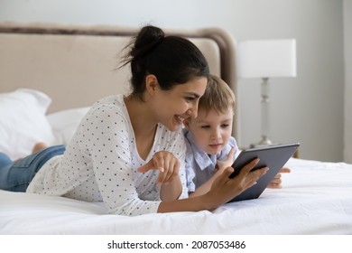 Caring smiling young Indian woman using digital computer tablet applications with happy small preschool kid son, playing games resting on bed, parental control, tech addiction concept. - Powered by Shutterstock