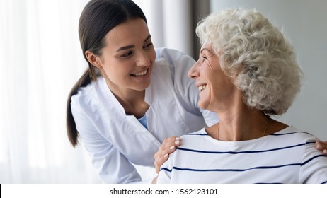 Caring Smiling Young Nurse Taking Care Supporting Happy Elder Grandma Patient, Female Doctor Caregiver Provide Medical Services Helping Old Woman At Homecare Medical Visit, Seniors Healthcare Concept