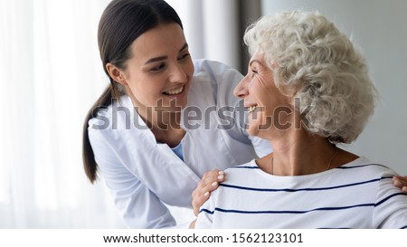 Caring smiling young nurse taking care supporting happy elder grandma patient, female doctor caregiver provide medical services helping old woman at homecare medical visit, seniors healthcare concept