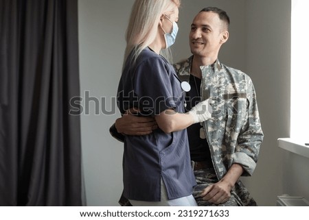 Caring wife nurse holding hands and supporting her military husband while talking to him in the hospital