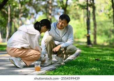 Caring young adult daughter tying her father shoelaces during their walk in the park - Powered by Shutterstock