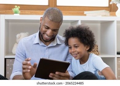 Caring young african american father using touchpad gadget with small adorable kid son, enjoying playing games online, watching funny cartoons or shopping in internet store, tech addiction concept. - Powered by Shutterstock