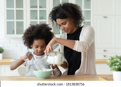 Caring young african american mother adding flour in bowl, helping little cute biracial kid daughter preparing homemade patisserie pastry or cooking pancakes for breakfast together in kitchen. - Powered by Shutterstock