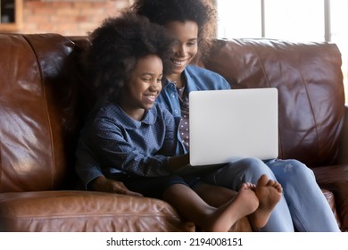 Caring Young African American Mother Teaching Little Child Daughter Using Computer Apps, Resting On Couch At Home. Addicted To Modern Technology Bonding Two Generations Diverse Family Playing Online