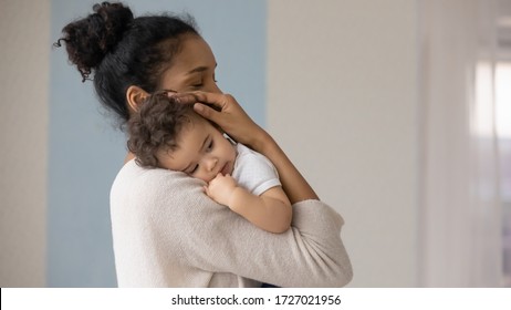 Caring young biracial mother hold lean to chest cute little infant toddler, loving african American mom hug embrace small baby child, relax enjoy tender family moment at home, childcare concept - Shutterstock ID 1727021956