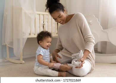 Caring Young Biracial Mother Sit On Warm Floor In Children Room Playing With Overjoyed Small Infant Toddler, Loving African American Mom Have Fun Entertain Little Ethnic Baby Child With Funny Toy