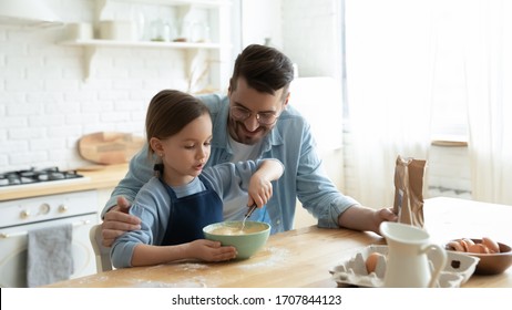 Caring young Caucasian dad and cute little preschooler daughter cooking in modern kitchen together, happy father and small girl child bake cookies pie, preparing pancakes for breakfast at home