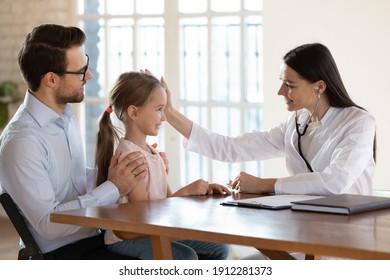 Caring young Caucasian female doctor cheer little girl child patient at hospital visit with dad. Attentive woman nurse or GP comfort caress small kid at consultation in clinic. Healthcare concept.