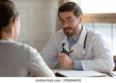 Caring Young Caucasian Male Doctor In White Medical Uniform Consult Female Patient Listen To Complaints. Man GP Have Consultation With Woman Client, Discuss Illness In Hospital. Healthcare Concept.