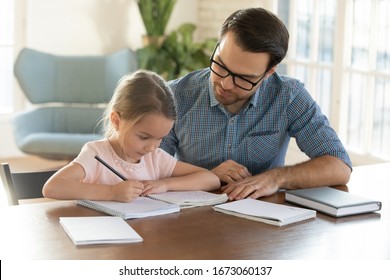 Caring young father helping little daughter and homework  Attentive small schoolgirl studying at home and young daddy  Dad teaching child writing letters in copy book  children education concept 