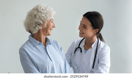 Caring young female caregiver in white coat smiling looking at old woman patient showing her support friendly attitude warm relation, nursing and healthcare, social homecare of elderly people concept - Powered by Shutterstock