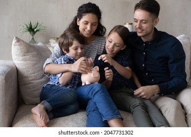 Caring Young Happy Couple Parents Teaching Small Children Son Daughter Saving Money For Future, Planning Own Budget Putting Coins In Small Piggybank Moneybox, Financial Literacy For Kids Concept.