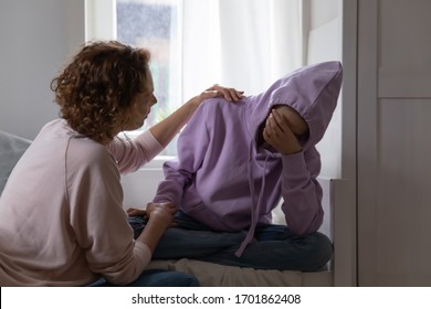 Caring Young Mother Comforting Sad Crying Teenage Daughter Sitting On Bed. Worried Adult Parent Mom Solacing, Apologizing Or Consoling Depressed Teen Girl Helping With Problem, Saying Sorry At Home.