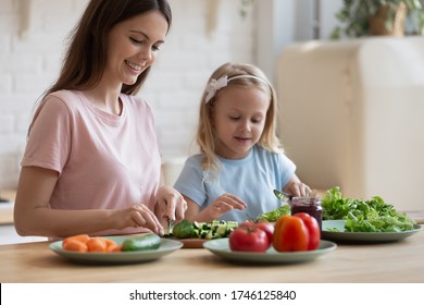 Caring Young Mother Have Fun Chop Vegetables Preparing Salad With Cute Little Daughter At Home, Loving Mom Or Nanny Cooking Breakfast Together With Small Preschooler Girl Child In Cozy Kitchen