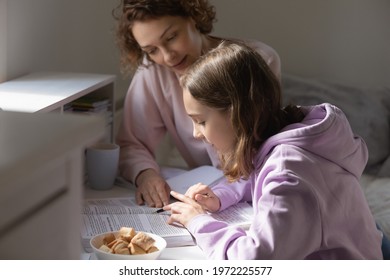 Caring young mother helping teenage kid daughter preparing for exams or checking homework indoors. Focused schoolgirl learning foreign language with mum, reading paper textbook, homeschooling concept. - Powered by Shutterstock