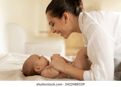 Caring young mother playing with her newborn baby daughter in the bed and looking at her with smile, happy moments of maternity - Powered by Shutterstock