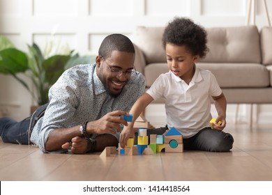 Caring young single black father help cute kid son play on warm floor together, happy african family dad and little child boy having fun building constructor tower from colorful wooden blocks