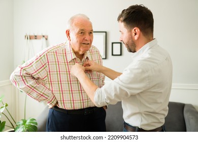 Caring young son helping his old happy elderly father to change clothes before going out of the house together