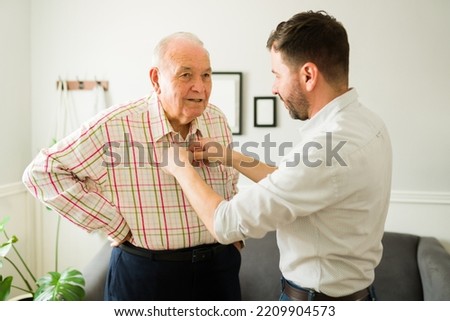 Caring young son helping his old happy elderly father to change clothes before going out of the house together