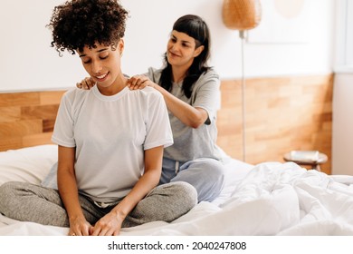 Caring young woman massaging her girlfriend at home. Romantic young woman giving her girlfriend a shoulder massage in their bedroom. Young LBGTQ+ couple bonding fondly on their bed.