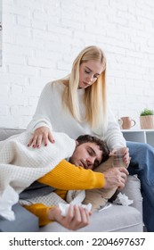 caring young woman sitting on sofa and giving glass of water to sick boyfriend - Shutterstock ID 2204697637