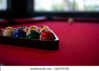 Carlsbad, California/United States - 07/23/19: A Dimly Lit Billiards Table, With  Racked Pool Balls, A Cue Ball, A Window In The Background, Red Felt - Pool Table