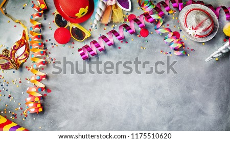 Carnival border of colorful streamers, confetti, hats, masks and sunglasses on grey with copy space for masquerade and party time