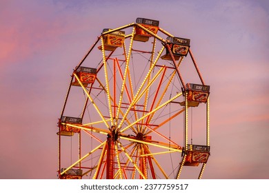 Carnival fairground Ferris wheel against pink sunset sky - Side on - Powered by Shutterstock